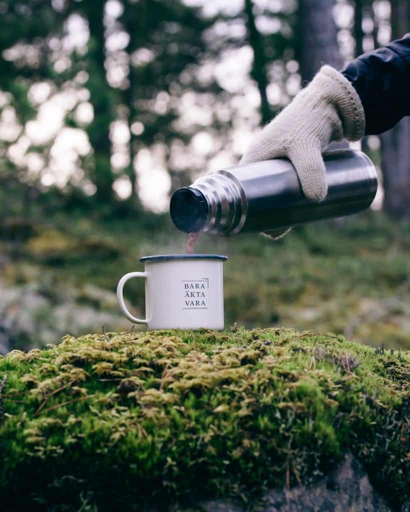 Pouring coffee from a thermos into an enamal mug out in nature.