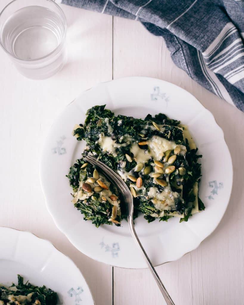 A plate with kale lasagna topped with pumpkin seeds